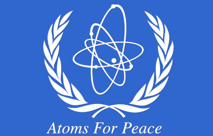 stylized atom centered between white wreaths 
on a field of UN blue, with motto: Atoms For Peace